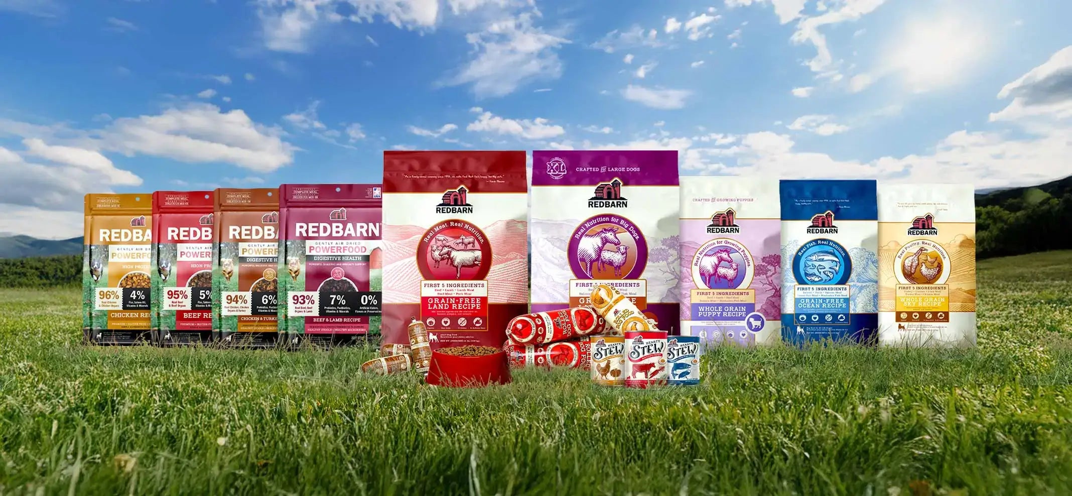 Assorted Redbarn pet food packages on grass with a blue sky background