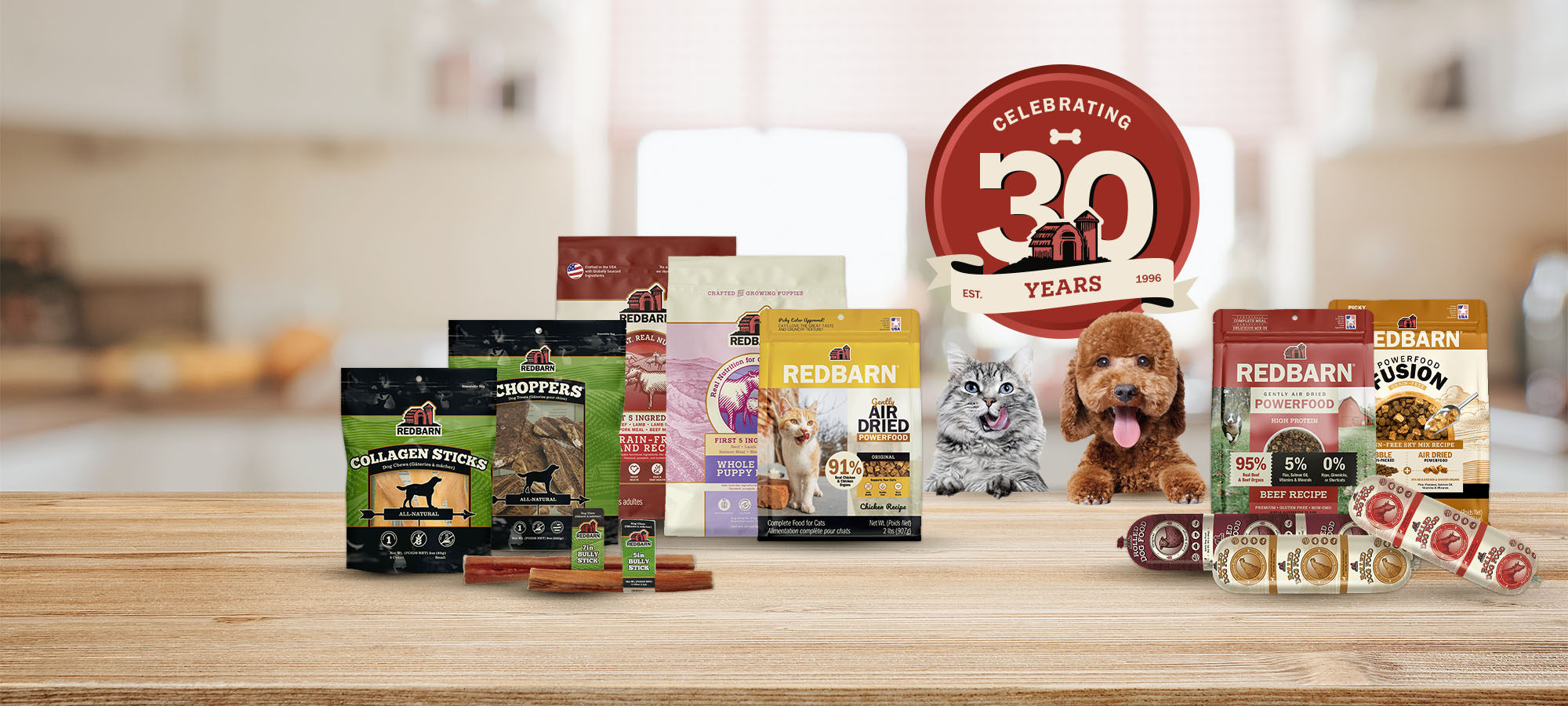 Assorted Redbarn pet food packages on a wooden surface with a 'Celebrating 30 Years' Redbarn logo.