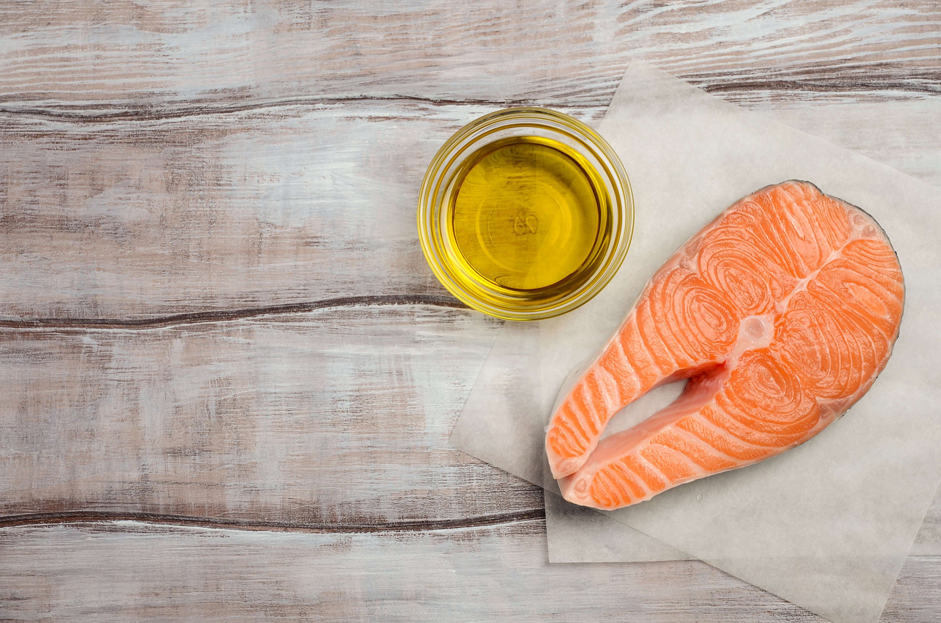 Raw salmon fillet with a glass of olive oil on a wooden surface